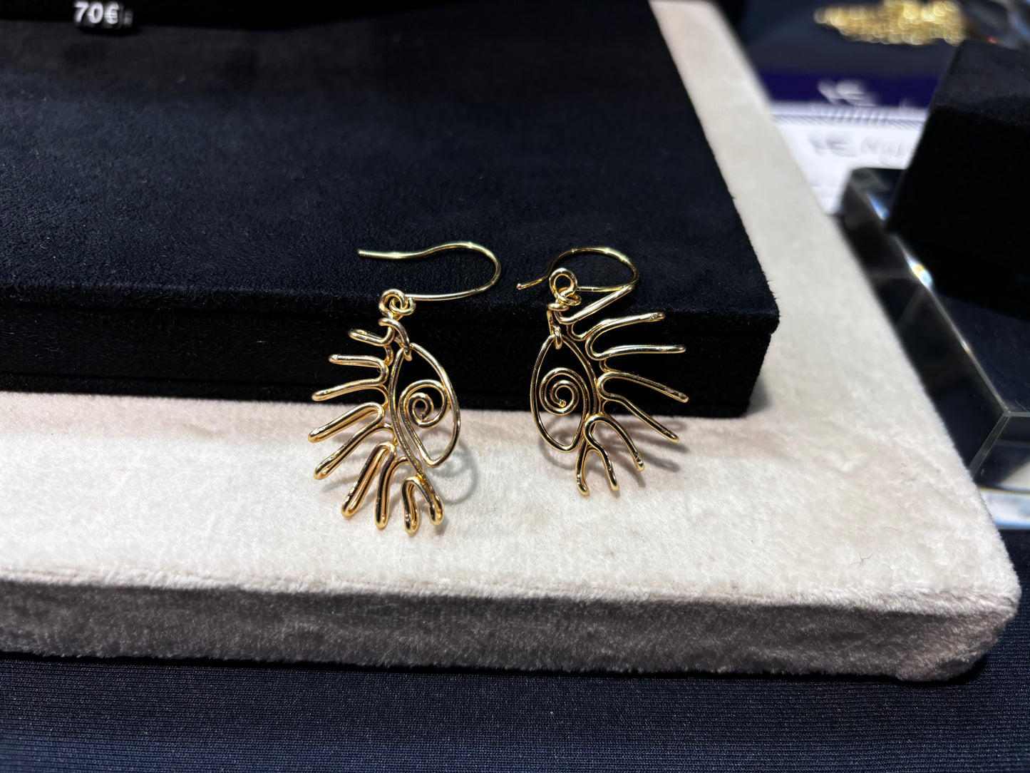 Boucles d’oreilles dorées avec un motif œil unique, suspendues à un présentoir élégant.