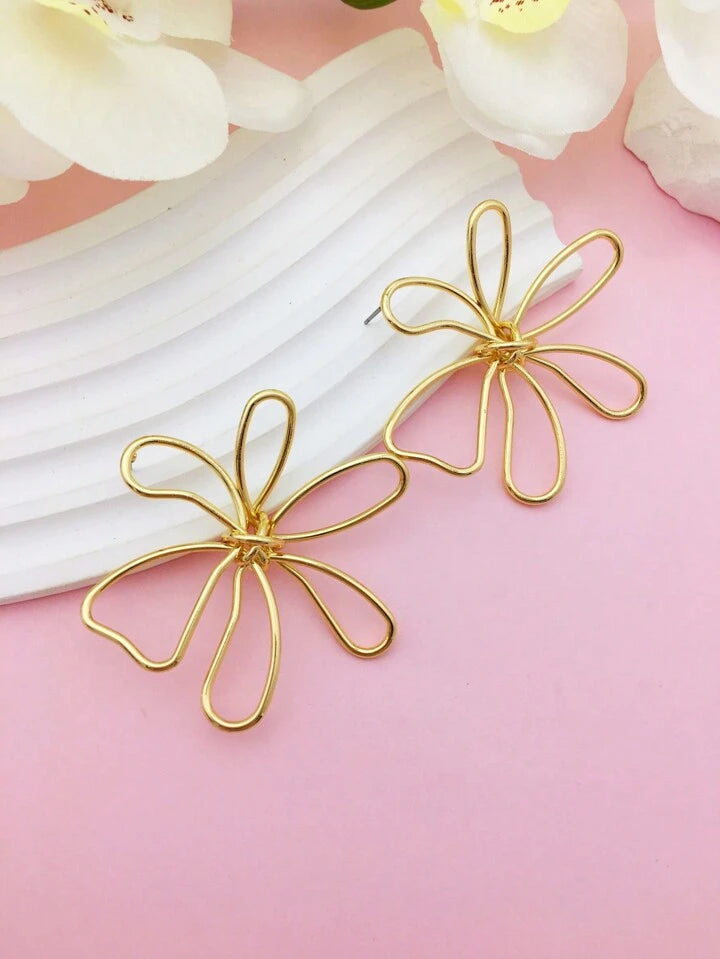 Paire de boucles d’oreilles fleuries en acier inoxydable 316L doré, exposées sur un fond rose.