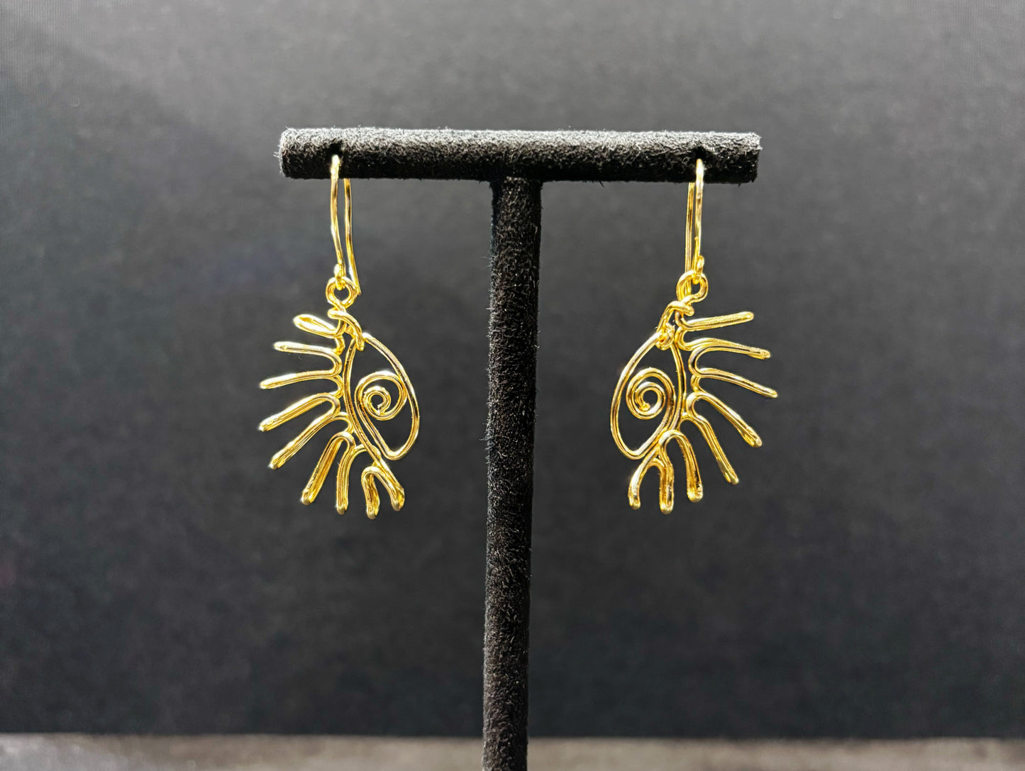 Paire de boucles d’oreilles motif œil en acier inoxydable doré, présentées sur un support noir