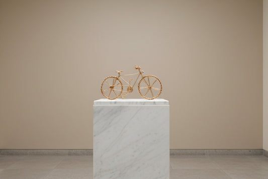 Sculpture de vélo en fil doré faite main, présentée sur un socle dans une ambiance galerie de luxe.