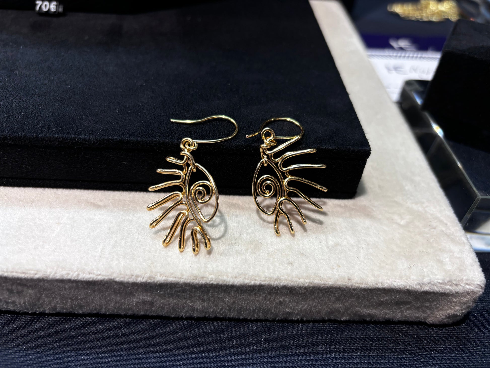 Boucles d’oreilles dorées avec un motif œil unique, suspendues à un présentoir élégant.