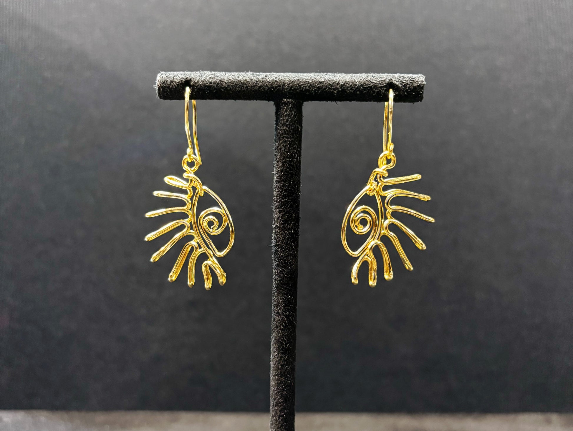 Paire de boucles d’oreilles motif œil en acier inoxydable doré, présentées sur un support noir