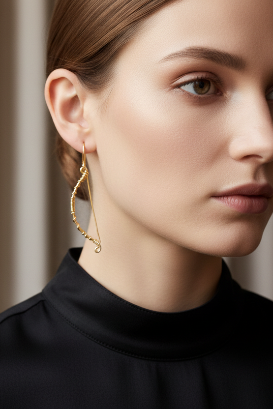 Femme élégante portant des boucles d’oreilles arc et flèche en fil métallique doré, design asymétrique fait main, bijou artisanal haut de gamme, création Najdovski Paris.