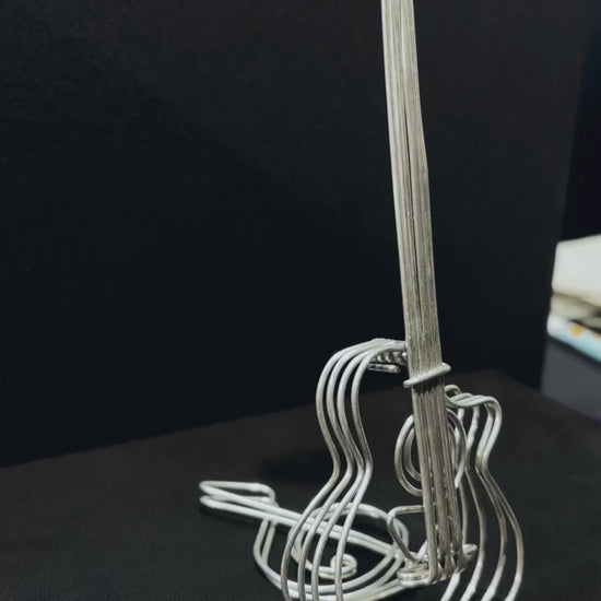 Vue rapprochée d’une sculpture en aluminium en forme de guitare, posée sur un fond noir élégant.