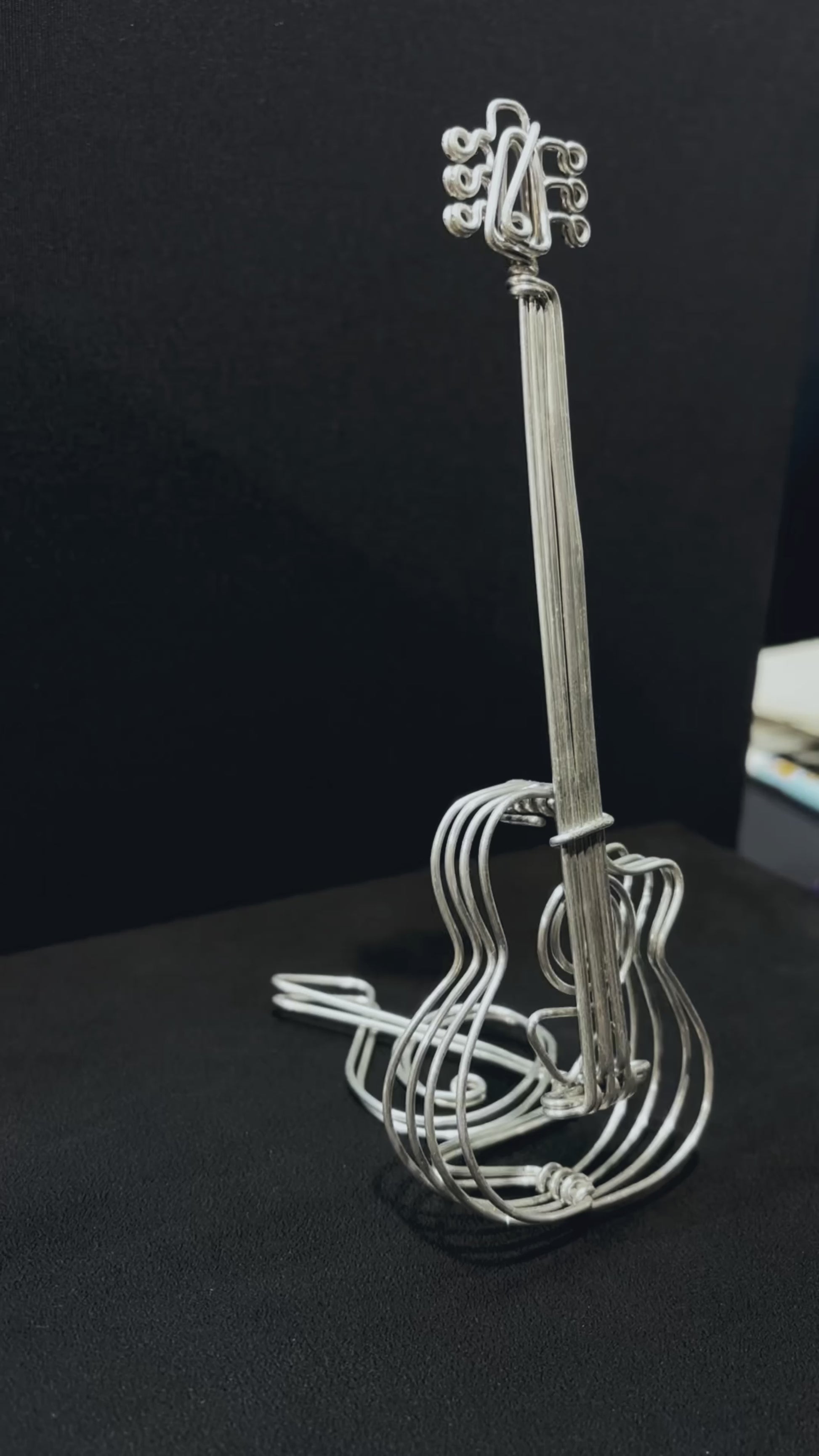 Vue rapprochée d’une sculpture en aluminium en forme de guitare, posée sur un fond noir élégant.