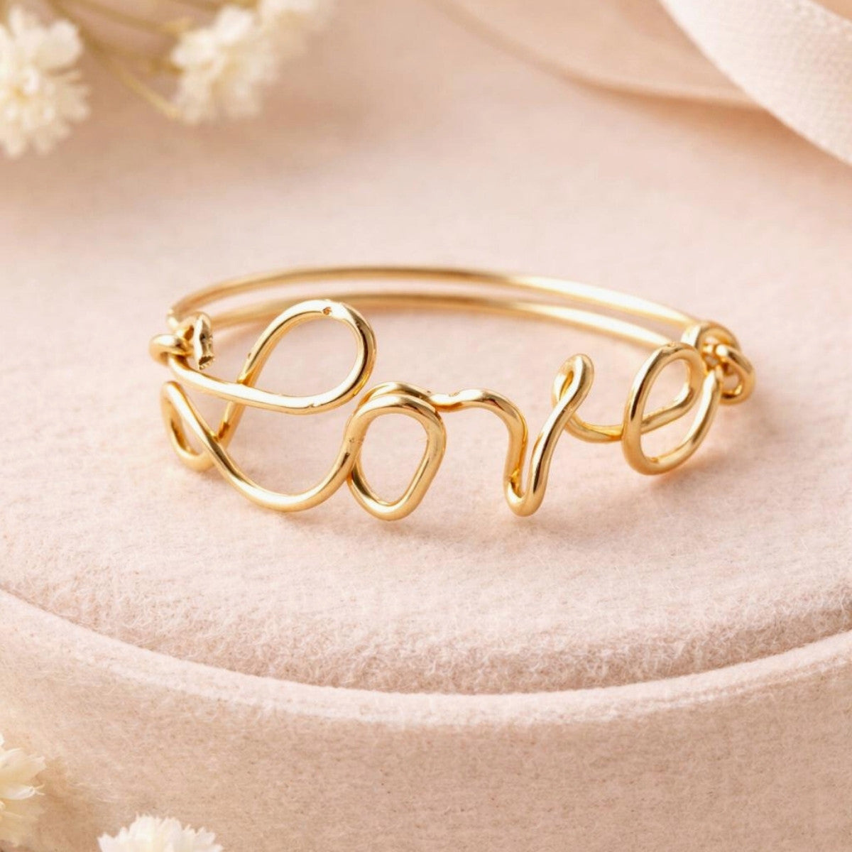 Bague prénom personnalisée en or posée sur un présentoir rose