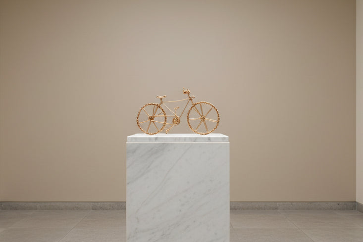 Sculpture de vélo en fil doré faite main, présentée sur un socle dans une ambiance galerie de luxe.
